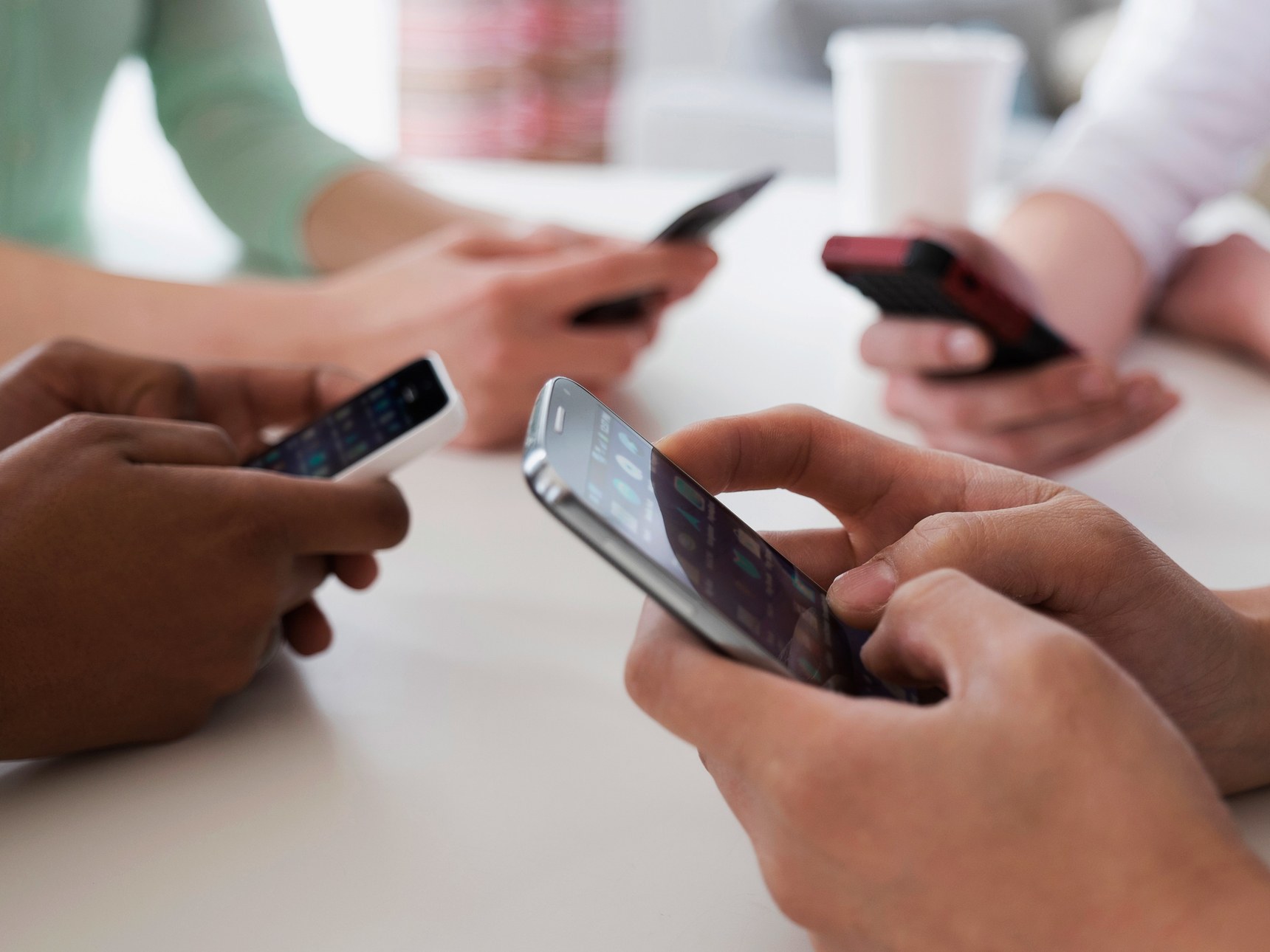 Close up of friends texting on cell phones at table