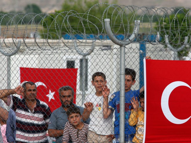 Migrants stand behind a fence at the Nizip refugee camp in Gaziantep province, southeastern Turkey, Saturday, April 23, 2016. German Chancellor Angela Merkel and top European Union officials, under pressure to reassess a migrant deportation deal with Turkey, are traveling close to Turkey's border with Syria on Saturday in a bid to bolster the troubled agreement. (AP Photo/Lefteris Pitarakis)
