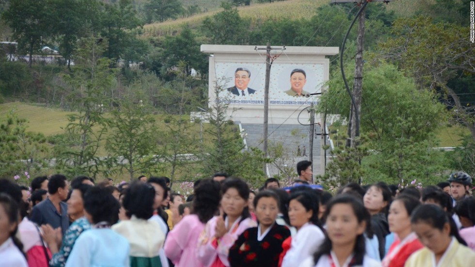 Spectators waiting for the bikers to reach the finish line. In the background the "Great" and "Dear Leaders" Kim Il Sung and his son, Kim Jong-Il.