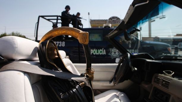 Federal police on patrol travel past a depiction of La Santa Muerte, or the Saint of Death, held in place by a seat belt in a car, during a rally in Ciudad Juarez June 19, 2011. More than 70 believers of Santa Muerte took part in the rally in Ciudad Juarez on Sunday to demand for increased security and a stop to violence in the city. REUTERS/Jose Luis Gonzalez (MEXICO - Tags: CIVIL UNREST CRIME LAW SOCIETY RELIGION IMAGES OF THE DAY) - RTR2NUUG