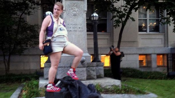 Claire Meddock, 21, stands on a toppled Confederate statue on Monday, Aug. 14, 2017, in Durham, N.C. Activists on Monday evening used a rope to pull down the monument outside a Durham courthouse. The Durham protest was in response to a white nationalist rally held in Charlottesville, Va, over the weekend. Authorities say one woman was killed Saturday after one of the white nationalists drove his car into a group of counterprotesters. (AP Photo/Jonathan Drew)