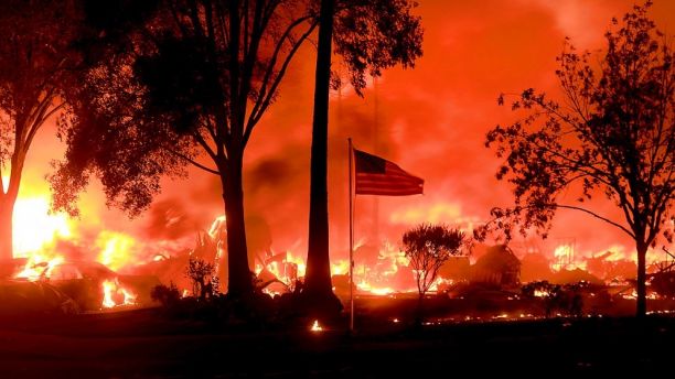 An American flag still fly's as as structures burn in Coffey Park, Monday Oct. 9, 2017. More than a dozen wildfires whipped by powerful winds been burning though California wine country. The flames have destroyed at least 1,500 homes and businesses and sent thousands of people fleeing. (Kent Porter/The Press Democrat via AP)