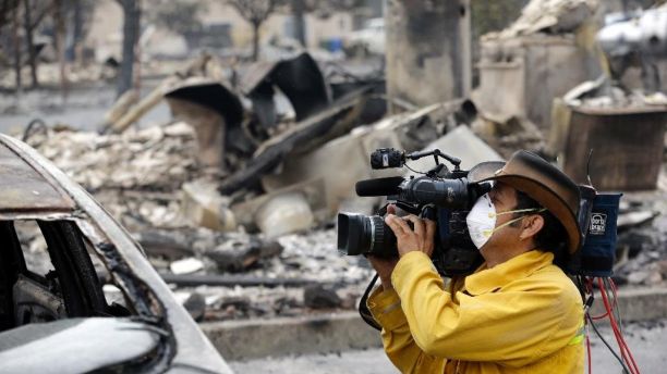 A video operator uses a mask as protetion against smoke and ash while filming the remains of an apartment building lost in a wildfire two days earlier, Monday, Sept. 14, 2015, in Middletown, Calif. Two of California's fastest-burning wildfires in decades overtook several Northern California towns, killing at least one person and destroying hundreds of homes and businesses and sending thousands of residents fleeing highways lined with buildings, guardrails and cars still in flames. (AP Photo/Elaine Thompson)