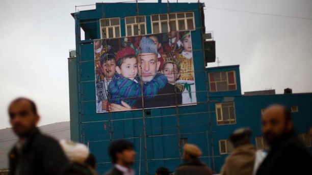 FILE - In this Nov 22, 2009, file photo, Afghan men waiting to get a ride out of the city queue next to a giant poster of Afghanistan's President Hamid Karzai in Kabul, Afghanistan. At least half the Afghan Taliban recently freed from Pakistani prisons have rejoined the insurgency, a Pakistani intelligence official said, complicating further releases and throwing into question the value of such goodwill gestures to restart a flagging peace process that shows no sign of ending a war that has raged for more than 11 years. (AP Photo/Anja Niedringhaus, File)