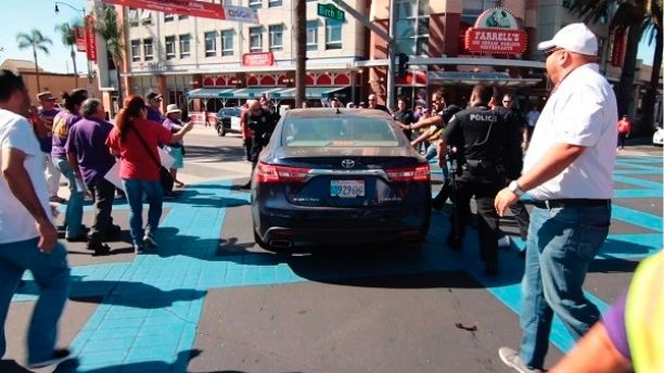 In this still image taken from video and released by Unite Here Local 11, Brea police officers rush to stop a motorist from driving his car into a crowd of people marching at an immigrant rights rally in Brea, Calif., Thursday, Oct. 26, 2017. Brea police Chief Jack Conklin said none of the demonstrators sought first aid. He said he did not know why the man drove through the intersection where people were gathered. Police arrested 56-year-old driver Daniel Wenzek for investigation of assault with a deadly weapon, said Lt. Adam Hawley. (Antonio Mendoza/Unite Here Local 11 via AP)