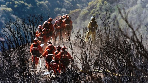 In this photo provided by the Santa Barbara County Fire Department, CAL FIRE Inmate Firefighting Hand Crew members hike through the charred landscape on their way to work east of Gibraltar Road above Montecito, Calif., Tuesday, Dec. 19, 2017. Officials estimate that the fire will grow to become the biggest in California history before full containment, expected by Jan. 7. (Mike Eliason/Santa Barbara County Fire Department via AP)