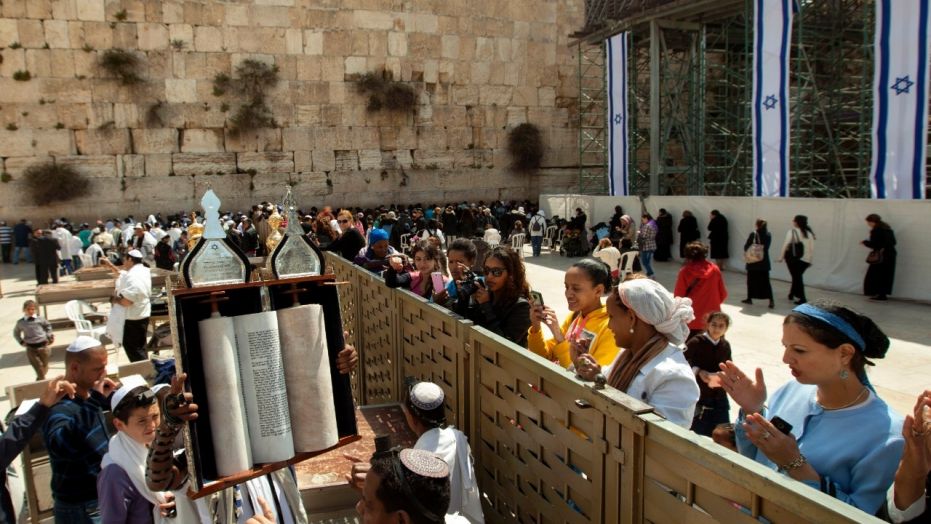 A man holds up a Torah scroll as women stand across a fence at the Western Wall, the holiest site where Jews can pray in Jerusalem's old city, Wednesday, April 10, 2013.