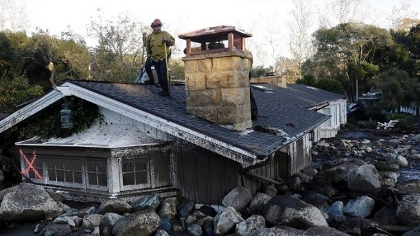 A firefighter stands on the roof of a house submerged in mud and rocks Wednesday, Jan. 10, 2018, in Montecito, Calif. Anxious family members awaited word on loved ones Wednesday as rescue crews searched grimy debris and ruins for more than a dozen people missing after mudslides in Southern California destroyed houses, swept cars to the beach and left more than a dozen victims dead. (AP Photo/Marcio Jose Sanchez)