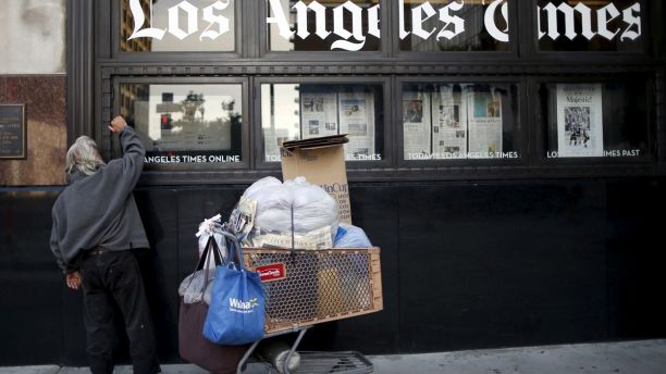 A homeless man reads the Los Angeles Times in the window of the building of Los Angeles Times newspaper, which is owned by Tribune Publishing Co, in Los Angeles, California, U.S., April 27, 2016. REUTERS/Lucy Nicholson - GF10000397617