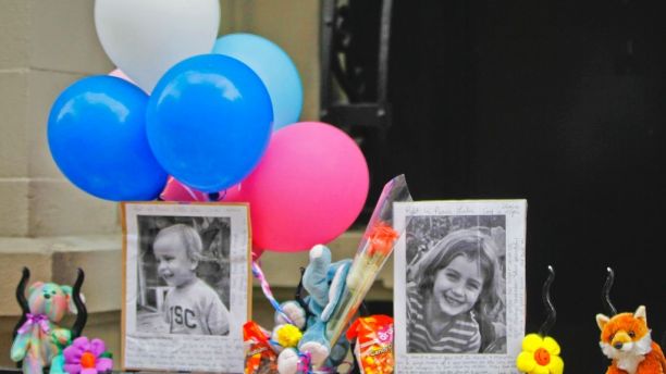 FILE - In this Oct. 27, 2012, file photo, photographs of 6-year-old Lucia Krim and her 2-year-old brother, Leo, are displayed alongside balloons and stuffed animals at a memorial outside the apartment building where they lived in New York. Opening arguments begin Thursday, March 1, 2018, for Yoselyn Ortega, the family's nanny charged with murder in the Oct. 25, 2012, deaths of the siblings. (AP Photo/Mary Altaffer, File)